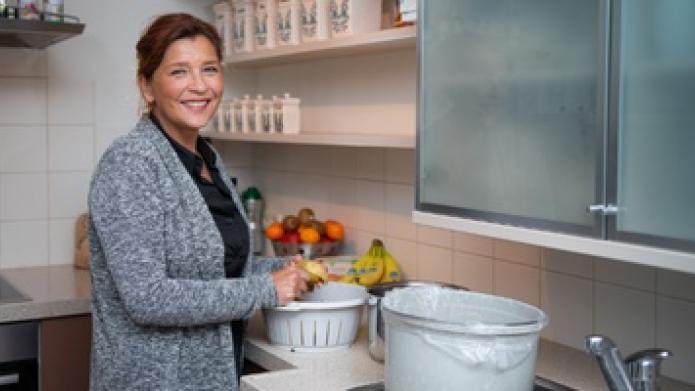 Monique van den Hombergh staat in haar keuken met een keukenafvalbakje voor gft. 